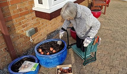 A gardener planting up containers with the kneeler and tool bag beside her